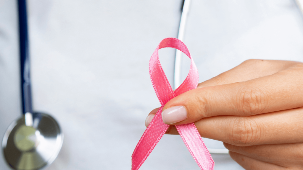 Imagem com uma pessoa vestida com jaleco e estetoscópio segurando um laço rosa em alusão ao outubro rosa
